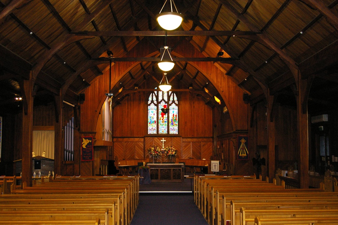 Intérieur d'une église avec de vastes panneaux en bois aux tons chauds, des poutres de plafond en bois apparentes et des bancs en bois.